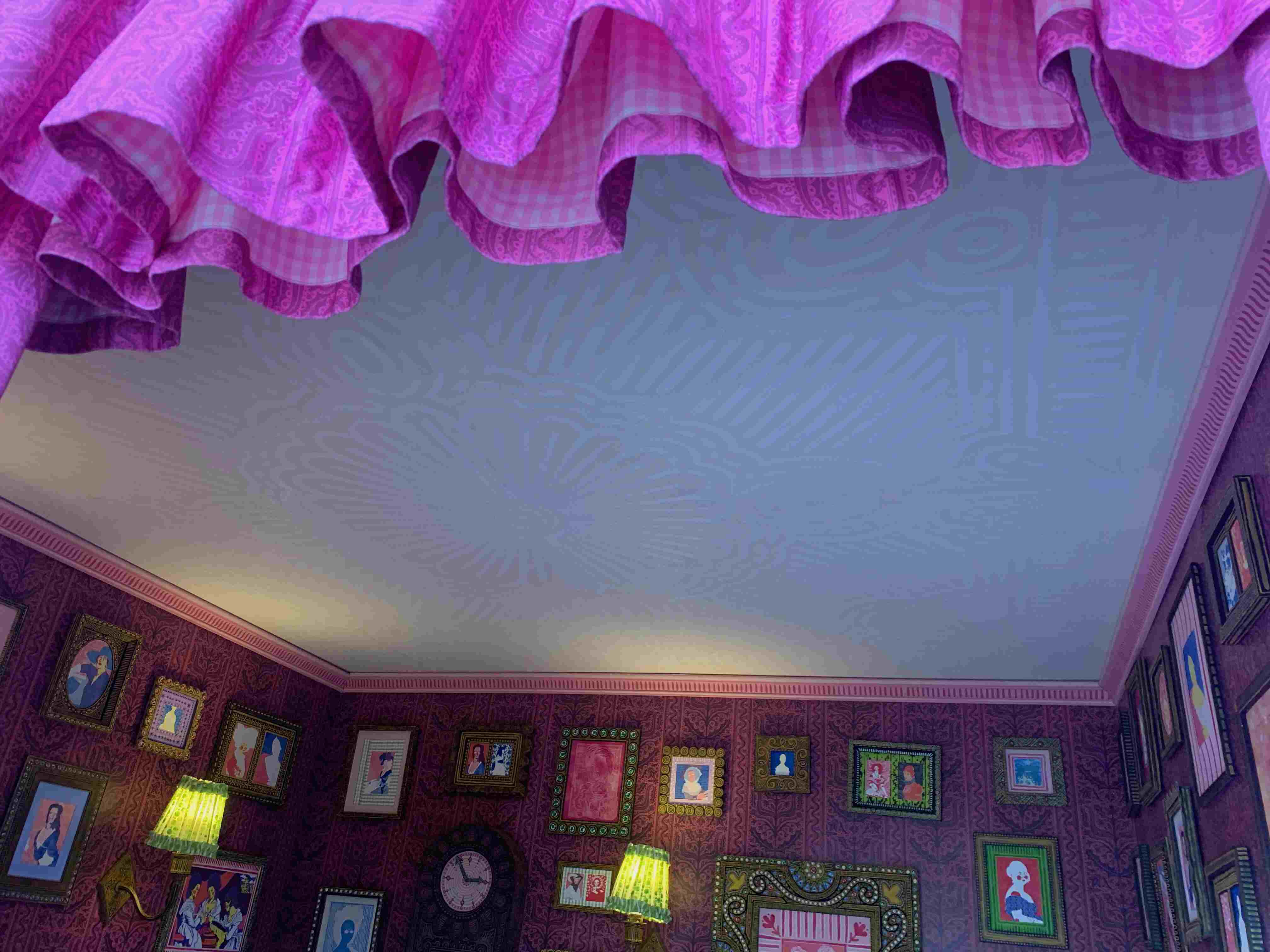pink room with a painted ceiling and wallpaper, sconce lights and frames on the walls