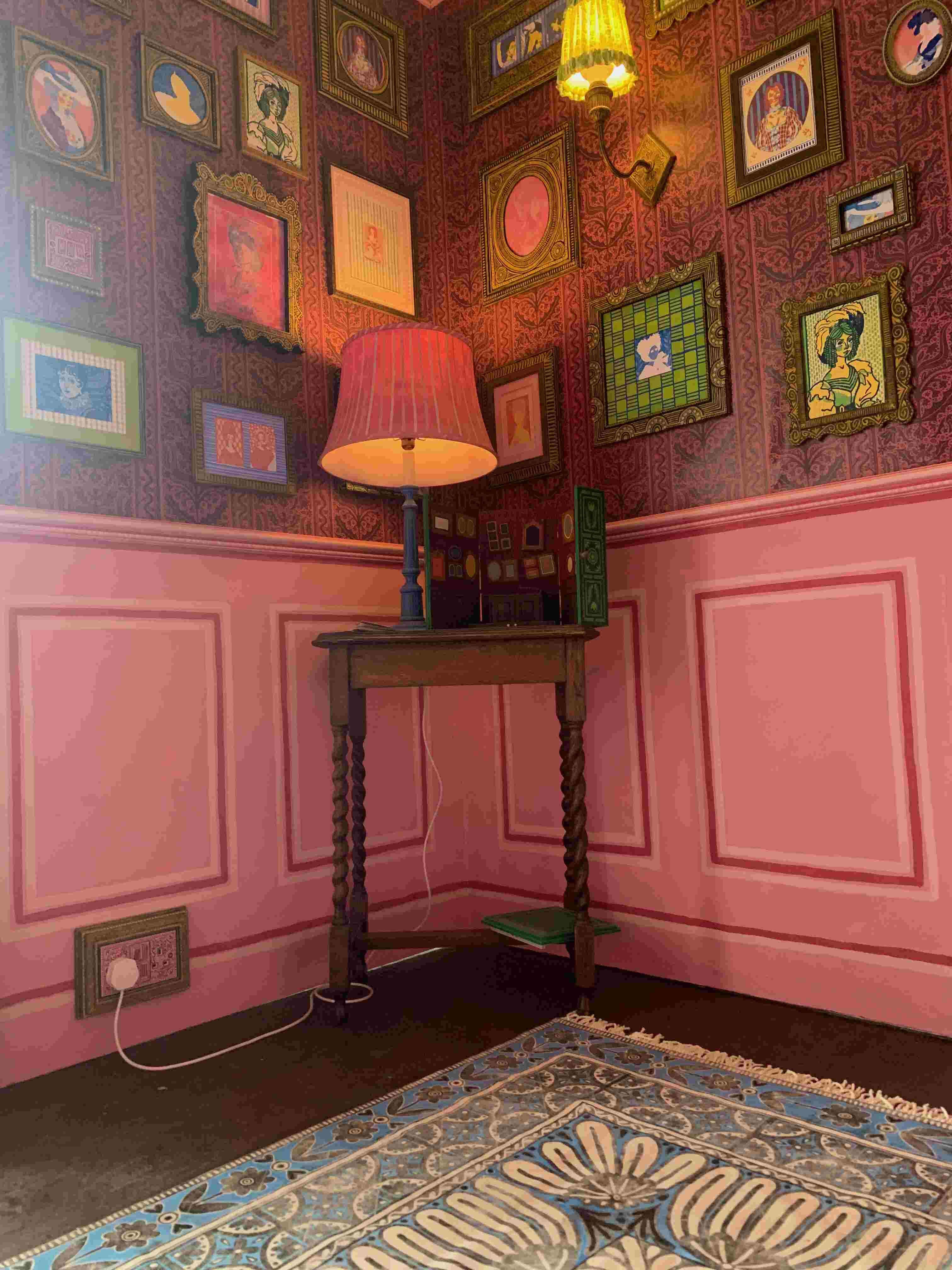 pink room with a painted ceiling and wallpaper, sconce lights and frames on the walls