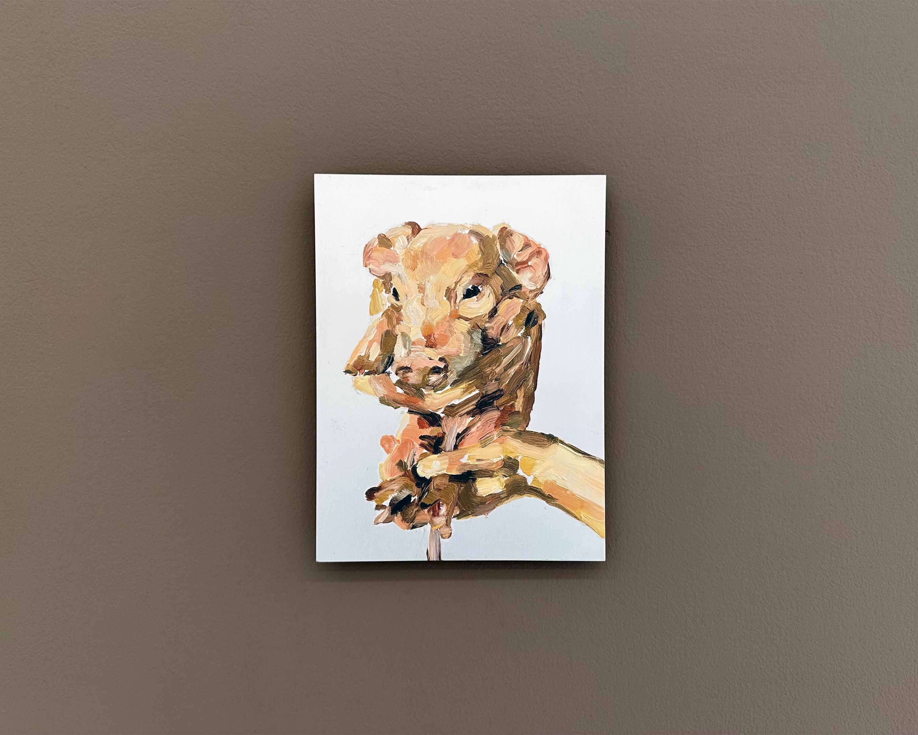painting on a piglet held in a hand on aluminium panel, on a brown wall
