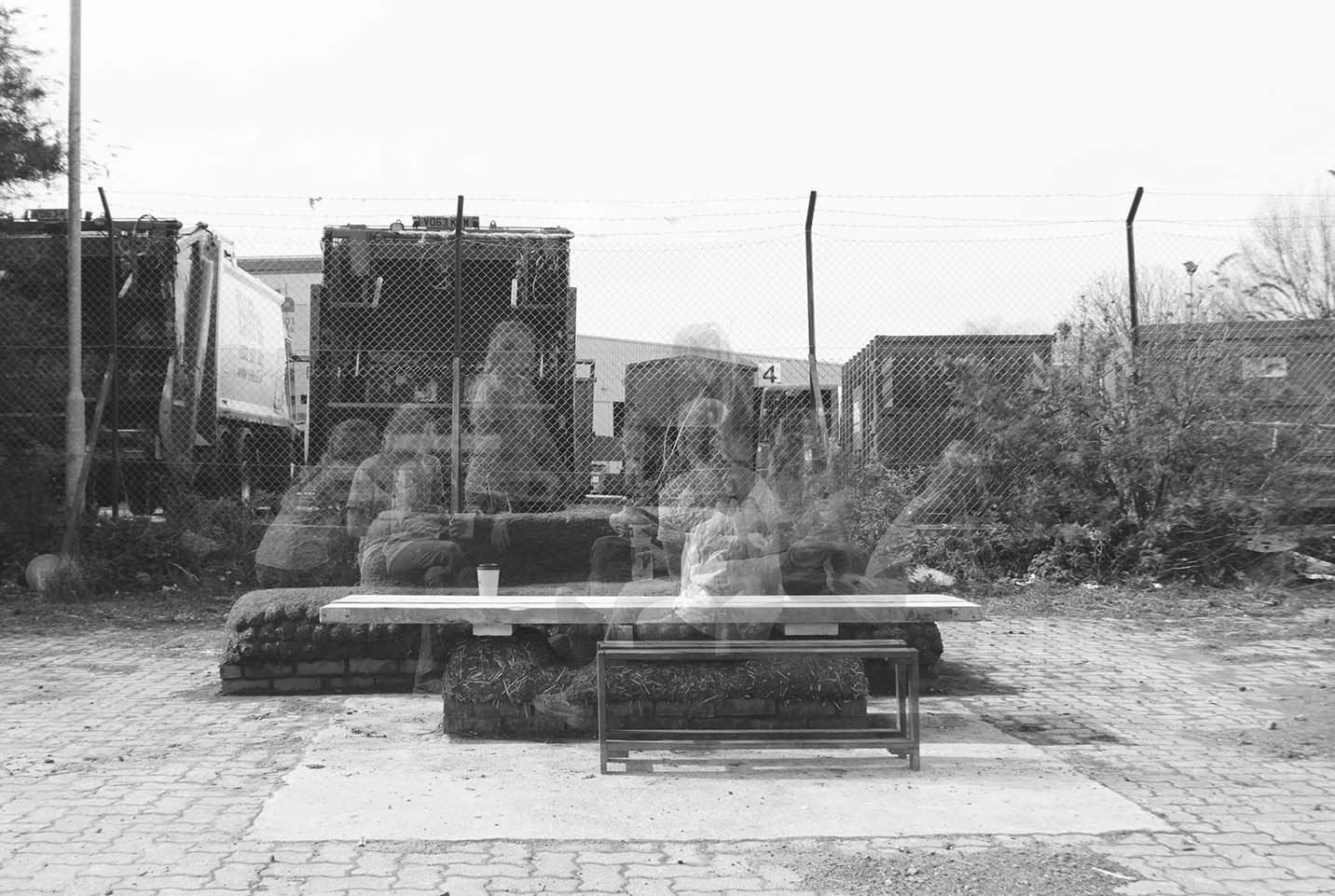 The Cobb in use: a mass earth bench and timber table sits on a vacant plot of land and many bodies and users are using it in diverse ways