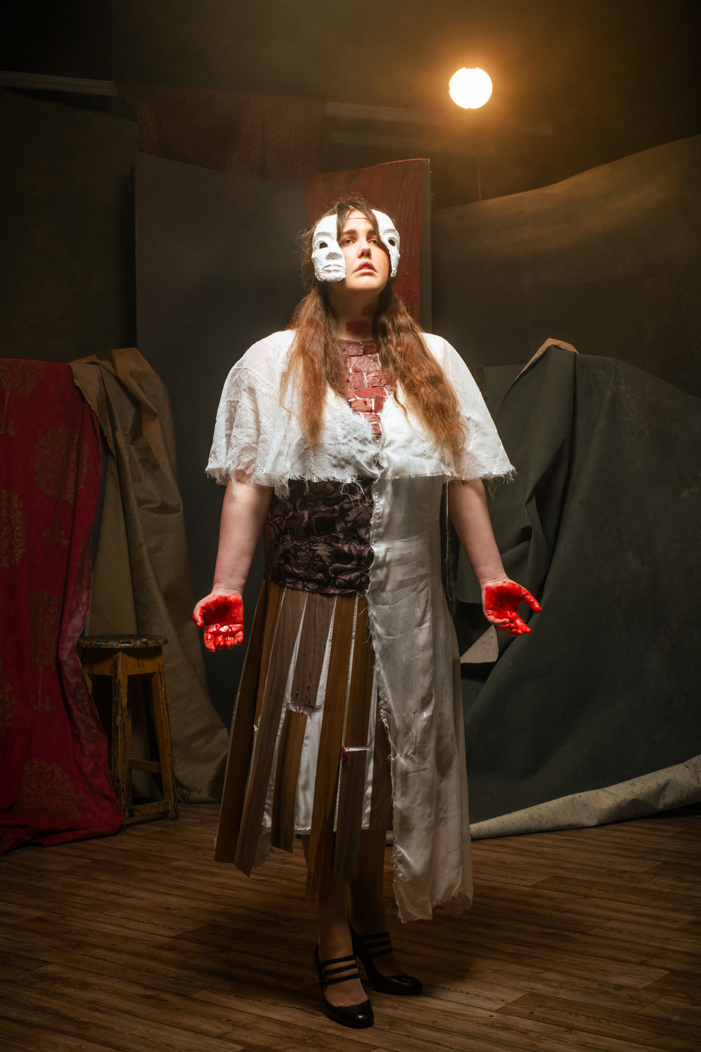 1920s dress imitating the bricks, wood planks, and wallpaper of a house. The performer wears a broken mask and her hands are stained with blood.