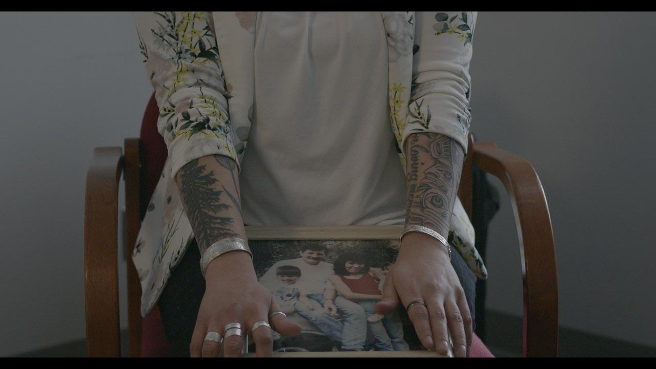 Women with tattoos holding a framed picture on her lap 