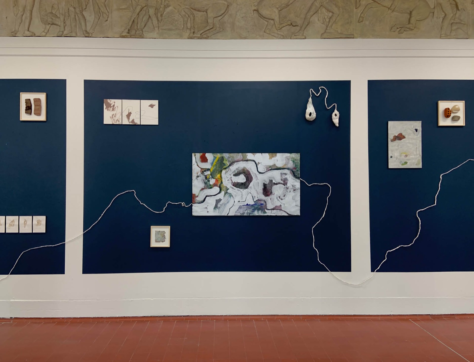 Paintings and drawings on deep blue squares with a sculptural line running across the installation