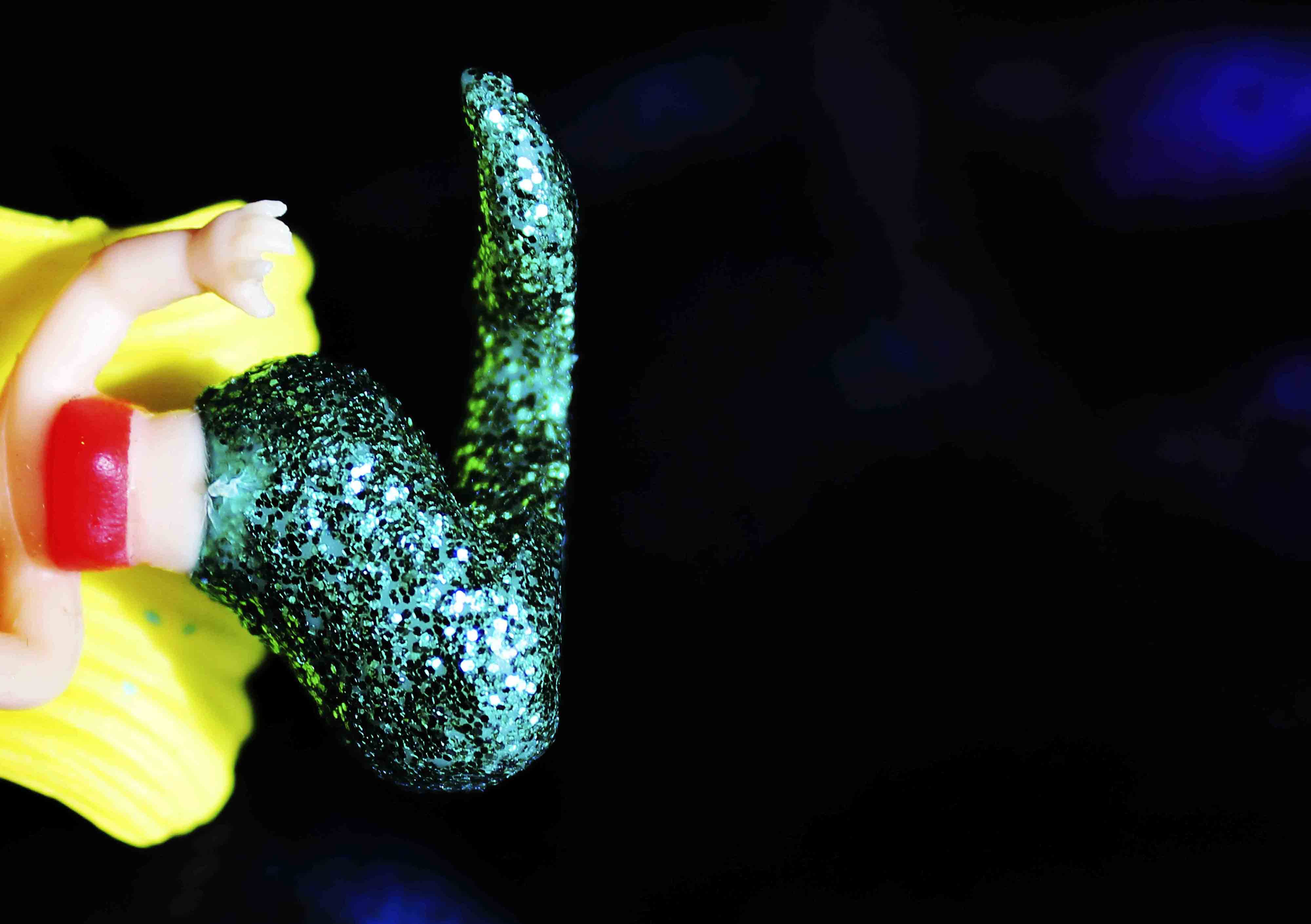 Image captures a miniature plastic toy mermaid with a green glittered tail and garish blonde hair.