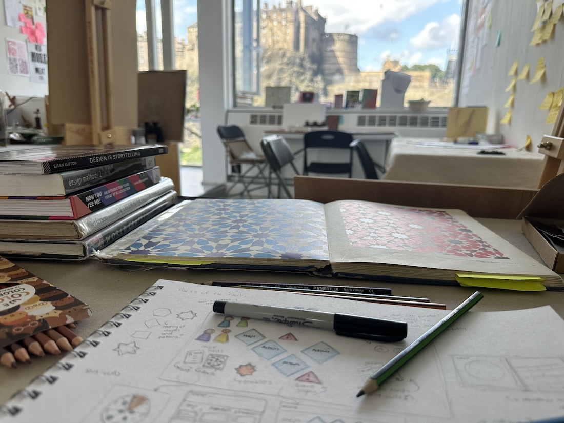 Desk with  a sketchbook, drawing tools and the Edinburgh Castle in the background